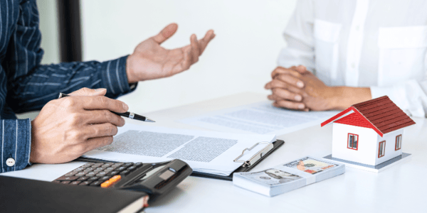 Two people talk over a contract with a calculator and some money on the table